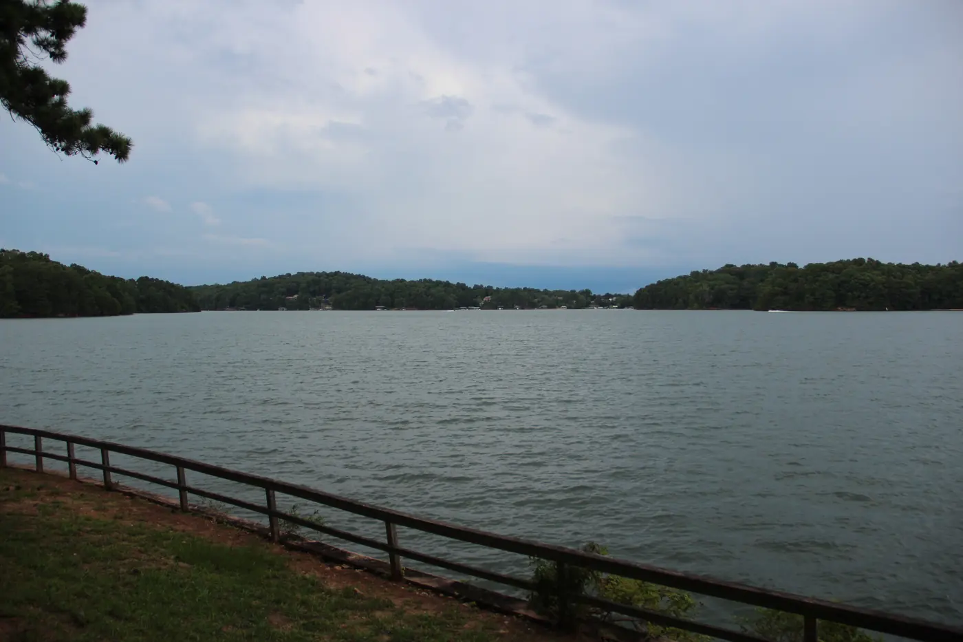 Wooden fence along a grassy bank overlooking a wide Lake Lanier cove with wooded shores under an overcast sky