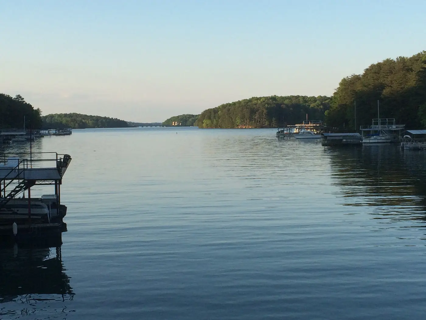Calm Lake Lanier cove in evening light with boat docks along the right shore and wooded hills in the distance